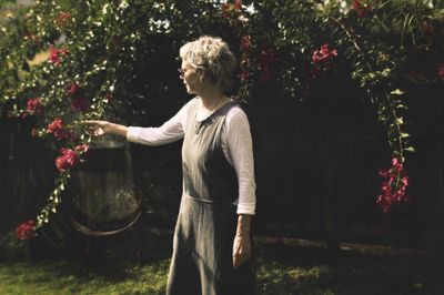 Woman in a garden reaching up to a flowering bougainvillea.