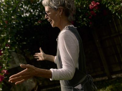 Older woman laughing with open hands in a flowering garden.